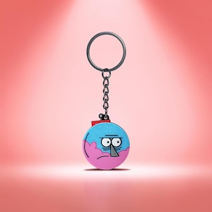 May include: A cartoon character keyring with a blue and pink spherical design and a grumpy face. The keyring has a silver metal ring and chain. The background is a gradient of pink and red.