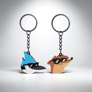 Peut inclure: Deux porte-clés représentant des personnages de dessins animés portant des lunettes de soleil. L'un est un oiseau bleu avec un bec noir et une poitrine blanche. L'autre est un hérisson brun. Les deux ont des porte-clés et des chaînes en métal noir.