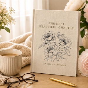 May include: A hardcover book with a beige linen-textured cover featuring the black text THE NEXT BEAUTIFUL CHAPTER and JENNIFER MARCHAND, accompanied by a black line-art illustration of a floral bouquet of peonies on the front cover.