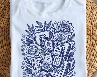 Può includere: T-shirt bianca con un design floreale blu con tessere di Mahjong. Il disegno include varie tessere con caratteri cinesi ed elementi floreali, creando un design dettagliato e artistico.