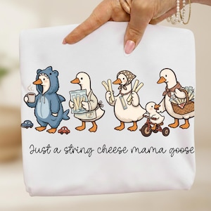 Könnte beinhalten: Weißer Stoff mit einer Cartoon-Illustration von Gänsen. Eine Gans trägt ein Haikostüm, andere tragen Käse oder fahren Dreirad. Der Text lautet "Just a string cheese mama goose."