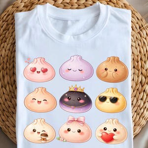 May include: White t-shirt featuring a colorful illustration of nine cartoon dumplings with various expressions and accessories. The dumplings are in shades of pink, purple, and brown, with details like hearts, sunglasses, and a crown.
