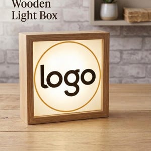 May include: A square wooden light box with the word "logo" in black letters inside a gold circle. The light box is illuminated, and the text "Personalized Wooden Light Box" is printed at the top.