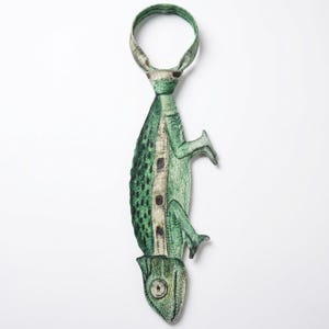 Op de afbeelding: Een novelty stropdas met een groen kameleonontwerp. De stropdas is voornamelijk groen met zwarte en witte accenten, en de kameleon is afgebeeld in een gedetailleerde, artistieke stijl. Een uniek accessoire.