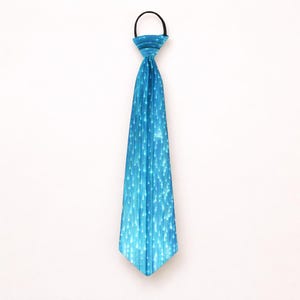 Peut inclure: Une cravate turquoise à clipser avec un motif de lignes verticales blanches. La cravate a une boucle élastique noire en haut pour une fixation facile. La cravate est de couleur unie avec un éclat subtil.