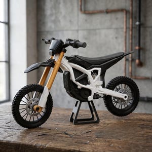 Könnte beinhalten: Ein Miniatur-Dirtbike-Modell mit weißem Rahmen, schwarzem Sitz und schwarzem Lenker. Die vorderen Federgabeln sind goldfarben und das Motorrad wird von einem schwarzen Ständer gehalten. Es hat schwarze Stollenreifen und silberne Scheibenbremsen.
