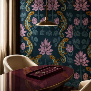 May include: A dark teal wallpaper featuring a repeating pattern of pink lotus flowers and orange lizards with blue spots. A gold pendant necklace and matching earrings are displayed on a dark red velvet tray atop a polished oval table.