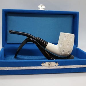 May include: A white tobacco pipe with a textured bowl and black stem, presented in a blue velvet box. The pipe has a unique design with a white band and is set against a light background.