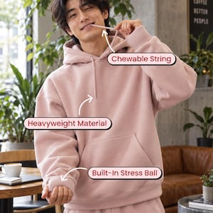 May include: A dusty pink hooded sweatshirt featuring a chewable string, heavyweight material, and a built-in stress ball inside the sleeve cuff. The hoodie includes a front kangaroo pocket and matching drawstring cords, providing a functional design.