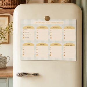 May include: A weekly planner magnet with a light blue and white gingham pattern is attached to a vintage fridge. The planner, titled "The 'Reality Check' Weekly Planner," has sections for each day of the week, with space for notes.