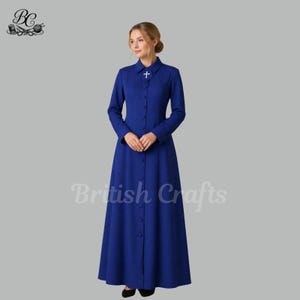 May include: A long, royal blue dress with a button-down front and a small white cross on the collar. The dress has long sleeves and a floor-length skirt. The text "British Crafts" is printed on the dress.