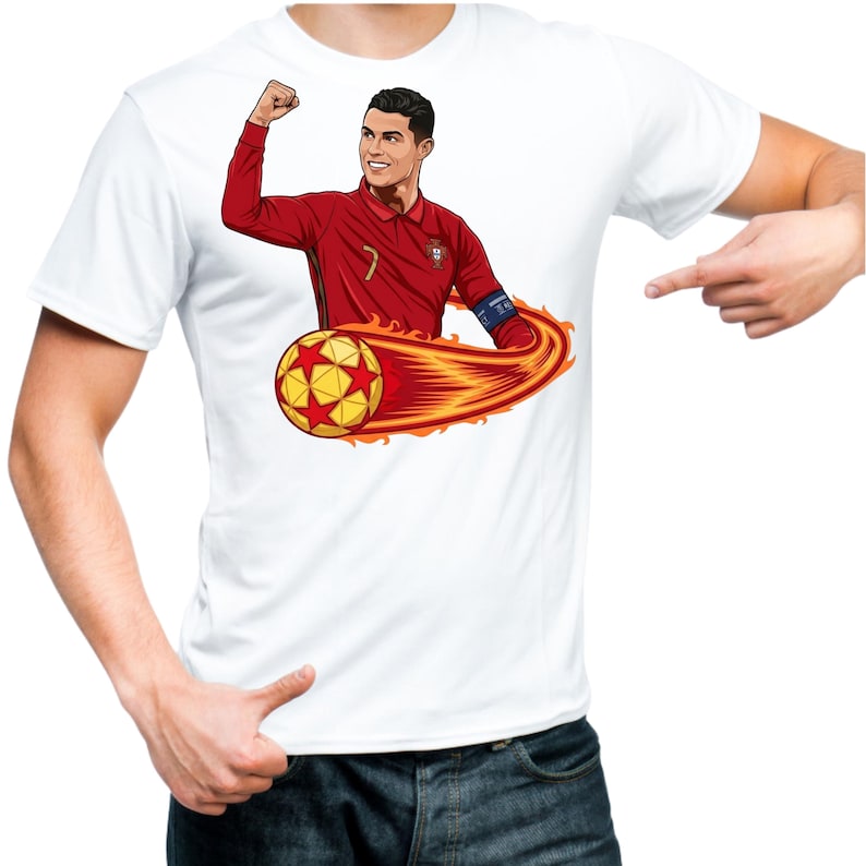 May include: White t-shirt featuring a cartoon illustration of a soccer player in a red jersey with a soccer ball engulfed in flames. The player is celebrating with a raised fist. The design is centered on the shirt.