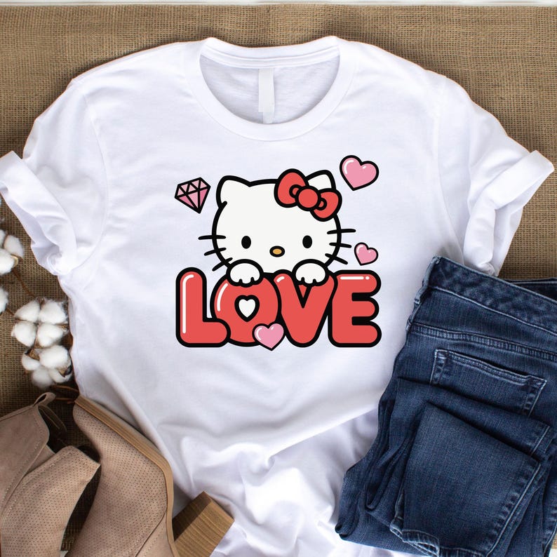 May include: White t-shirt featuring a graphic of a cartoon cat with a red bow, surrounded by hearts and a diamond. The word "LOVE" is displayed in red, with a pink heart in the center of the "O".