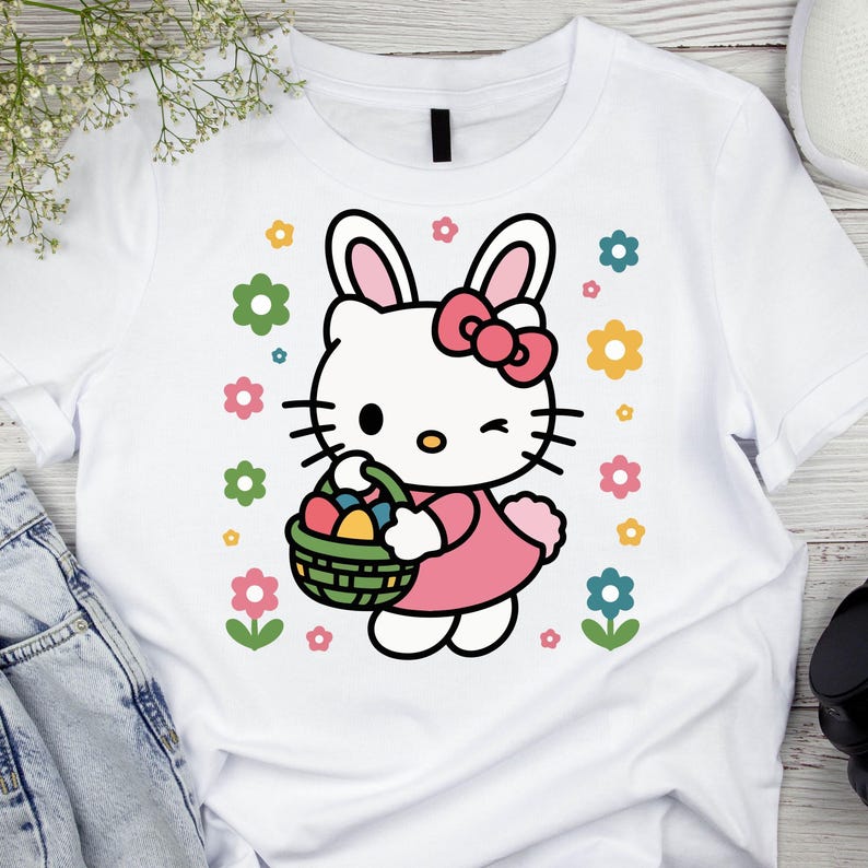 May include: White t-shirt featuring a cartoon character with bunny ears, a pink bow, and a pink dress, holding a basket of Easter eggs. Colorful flowers surround the character. The shirt is made of a soft material.