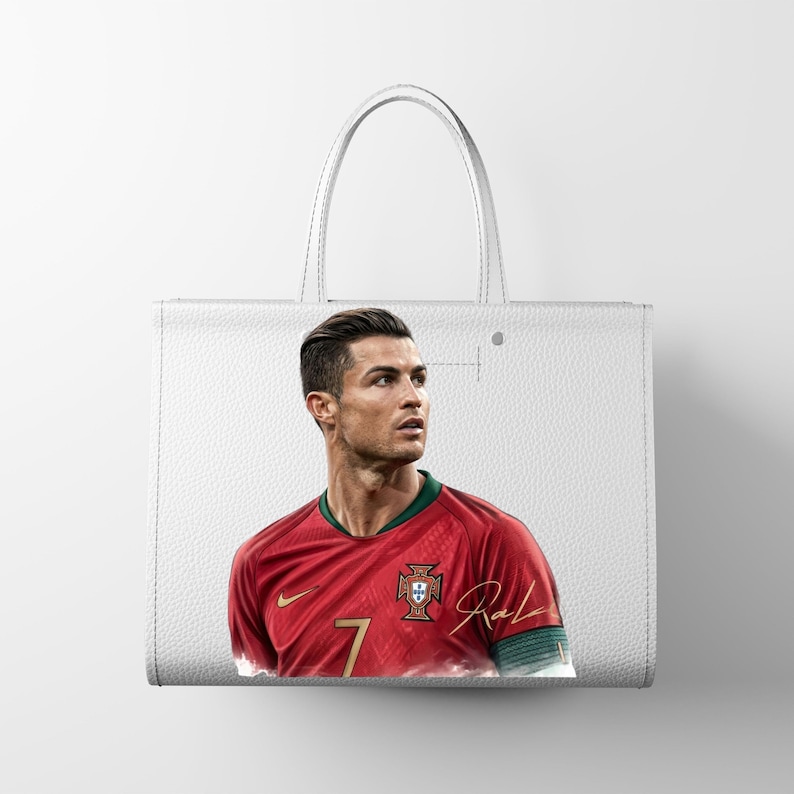 May include: White tote bag featuring a portrait of a soccer player in a red jersey with the number 7. The bag has a leather-like texture and a simple design, with a handle for carrying.