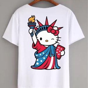 May include: White t-shirt featuring a cartoon illustration of Hello Kitty dressed as the Statue of Liberty. The design includes a red bow, a torch with a flame, and a tablet with stars, all in patriotic colors.