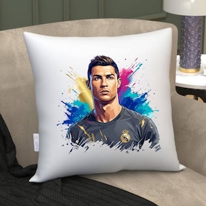 May include: White square throw pillow featuring a portrait of a man with dark hair and a serious expression. The image is set against a colorful splash of blue, pink, and gold. The man is wearing a gray shirt with a gold emblem.