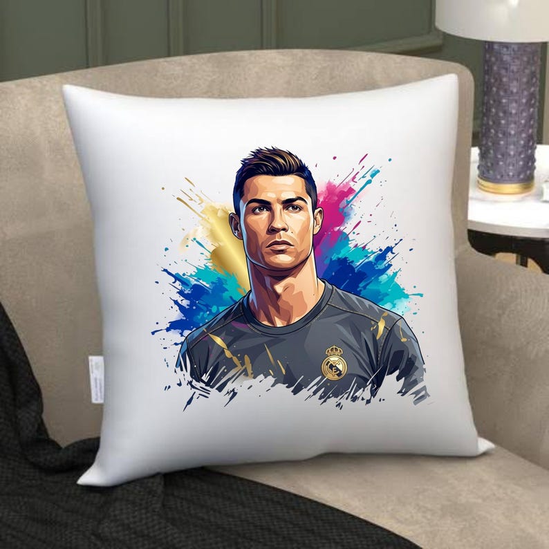 May include: White square throw pillow featuring a portrait of a man with dark hair and a serious expression. The image is set against a colorful splash of blue, pink, and gold. The man is wearing a gray shirt with a gold emblem.