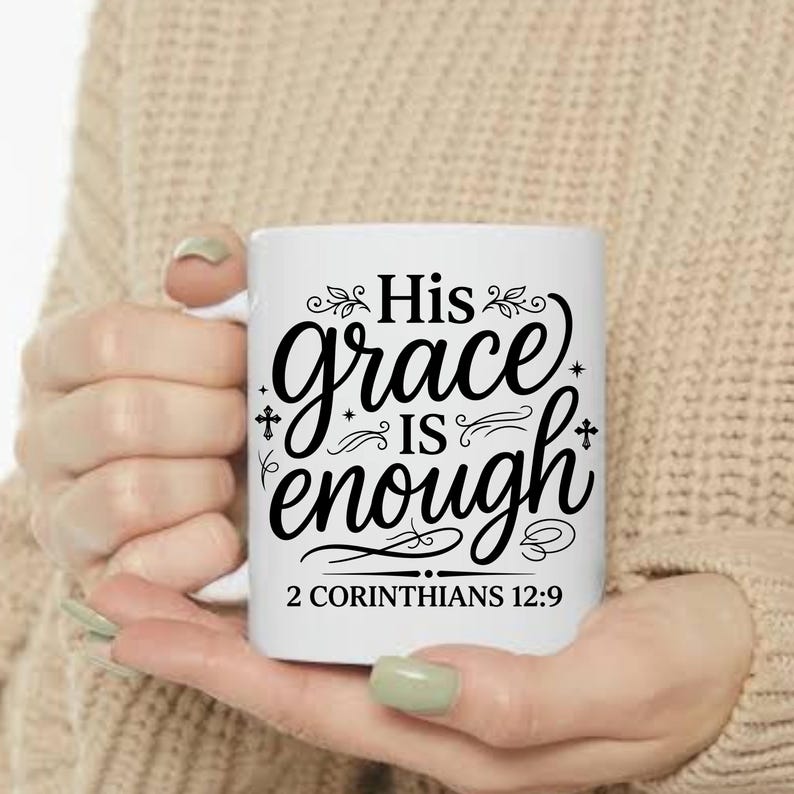 May include: White ceramic mug with the text "His grace is enough" in black script. The mug also features the Bible verse "2 Corinthians 12:9". The mug is held in a person's hands.