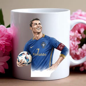 May include: White ceramic mug featuring a portrait of a soccer player in a blue jersey with the number 7 and the name "Ronaldo". The player is holding a soccer ball and smiling. The mug has a handle on the right side.
