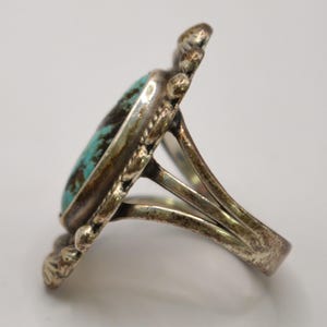 Puede incluir: Un anillo de plata con una piedra turquesa ovalada con patrones de matriz de color marr&oacute;n oscuro. El engaste de metal tiene un borde festoneado decorativo con peque&ntilde;os detalles de cuentas. La banda se divide en tres secciones distintas.