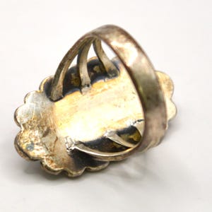 Puede incluir: Un anillo de metal plateado con un engaste de borde festoneado y una banda de v&aacute;stago dividido. La superficie met&aacute;lica muestra una p&aacute;tina envejecida y deslustrada con oxidaci&oacute;n oscura visible en las &aacute;reas hundidas alrededor de la placa central.