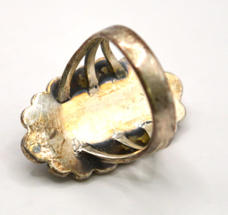 Puede incluir: Un anillo de metal plateado con un engaste de borde festoneado y una banda de v&aacute;stago dividido. La superficie met&aacute;lica muestra una p&aacute;tina envejecida y deslustrada con oxidaci&oacute;n oscura visible en las &aacute;reas hundidas alrededor de la placa central.