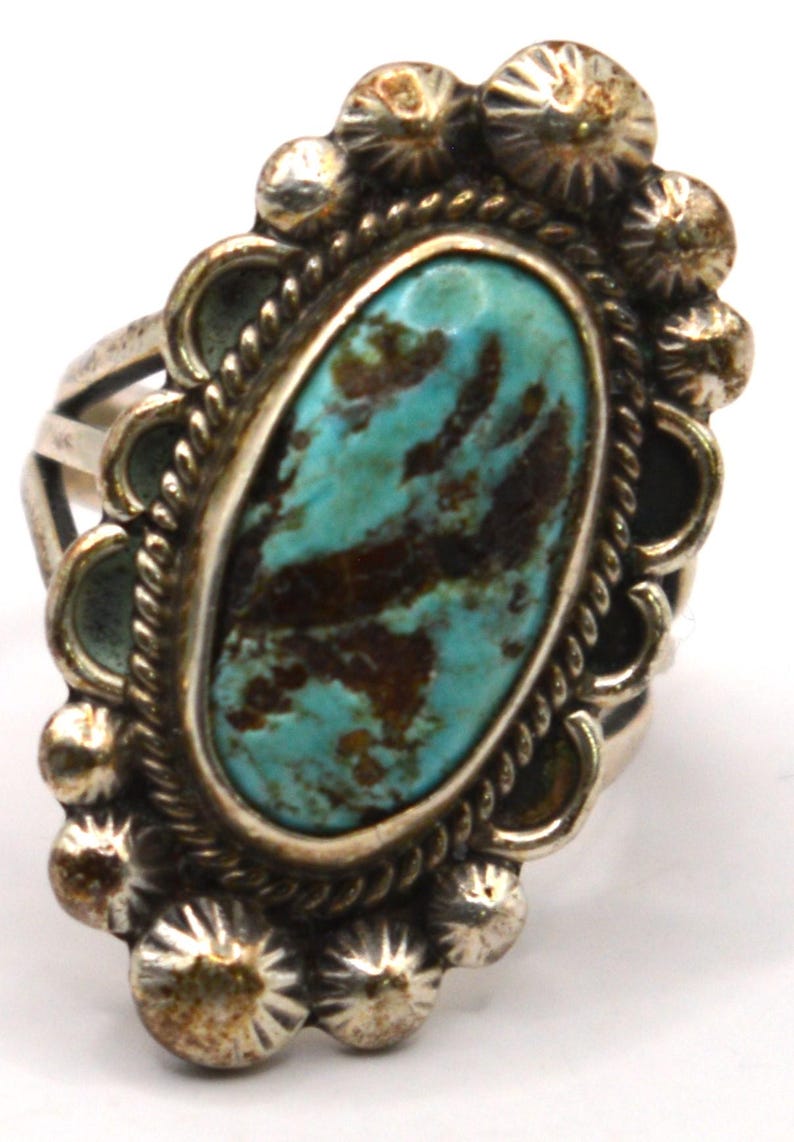 Puede incluir: Un anillo de plata con una piedra turquesa de forma ovalada con patrones de matriz de color marr&oacute;n oscuro. La piedra est&aacute; rodeada por un borde de cuerda trenzada y un borde festoneado adornado con peque&ntilde;as cuentas de plata redondas.