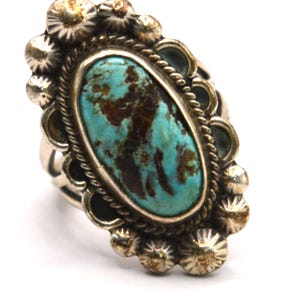 Puede incluir: Un anillo de plata con una gran piedra turquesa de forma ovalada con patrones de matriz de color marr&oacute;n oscuro. La piedra est&aacute; rodeada por un borde de cuerda trenzada y un marco de plata festoneado con peque&ntilde;as cuentas de plata texturizadas.