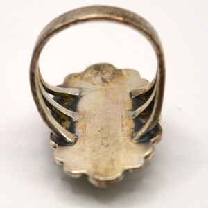Puede incluir: Un anillo de tono plateado con un engaste ovalado festoneado y un acabado oscuro y deslustrado en la parte inferior. La banda est&aacute; formada por tres hilos plateados finos y paralelos que se conectan a la parte posterior de la placa central.