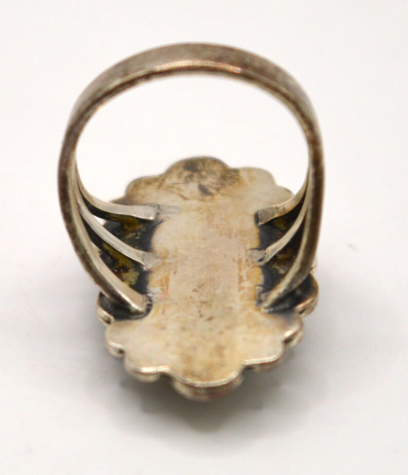 Puede incluir: Un anillo de tono plateado con un engaste ovalado festoneado y un acabado oscuro y deslustrado en la parte inferior. La banda est&aacute; formada por tres hilos plateados finos y paralelos que se conectan a la parte posterior de la placa central.