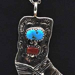 May include: Silver pendant necklace featuring a cowboy boot design. The boot pendant is adorned with a turquoise stone and a red stone. The necklace has a delicate chain and a simple clasp.