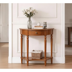 May include: A wooden, half-moon console table with a drawer and lower shelf. The table has turned legs and a warm brown finish. A woven basket sits on the shelf. A vase of flowers and decorative items are on the tabletop.