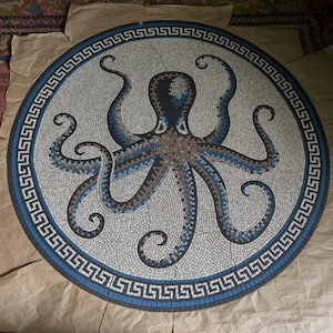 May include: A circular mosaic tile featuring an octopus design. The octopus is depicted in shades of blue, brown, and black against a white background. The mosaic is framed by a blue and white Greek key border.
