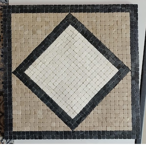 Puede incluir: Un panel de mosaico cuadrado que presenta una forma de diamante central blanca rodeada por un borde negro, sobre un fondo de azulejos beige claro, todo enmarcado por un perímetro exterior de pequeñas baldosas de piedra negras y cuadradas.