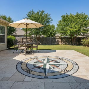 May include: Outdoor patio with a compass rose mosaic inlay. A round table and chairs are under a beige umbrella. The patio is surrounded by a green lawn and trees, with a clear blue sky overhead.