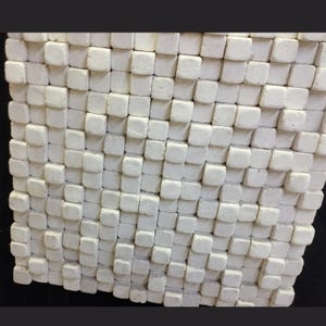 May include: A square wall panel composed of numerous small, off-white, matte-finished cubes arranged in a grid pattern. Each individual cube has slightly rounded edges and a textured surface, creating a uniform, three-dimensional geometric relief.