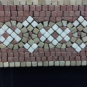 May include: A rectangular stone mosaic border featuring a repeating pattern of interlocking circles and diamonds. The design is composed of small, square-cut tiles in shades of deep red, beige, and white, arranged in a structured, geometric layout.