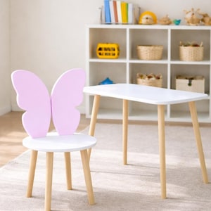 May include: A white table with four light wood legs and a matching chair featuring a backrest shaped like two light pink butterfly wings. The chair has a round white seat and four light wood legs that match the table's design and construction.