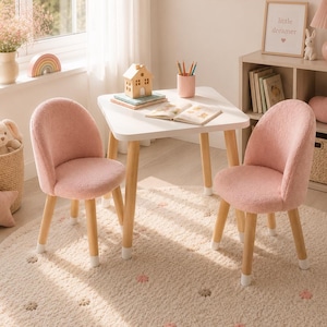 May include: A white square table with four light wood legs and two matching pink upholstered chairs with textured fabric. The table holds a small wooden house, a pink pencil holder with colored pencils, and an open book. The set sits on a round rug.