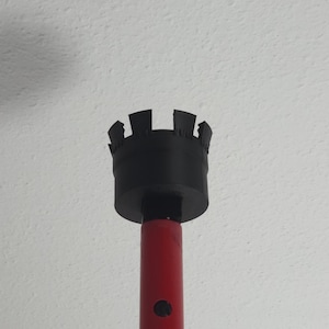 Peut inclure: Un outil rouge et noir avec une poignée cylindrique rouge et une tête noire en forme de couronne. La tête comporte de multiples découpes rectangulaires. Un petit bouton noir est visible sur la poignée.