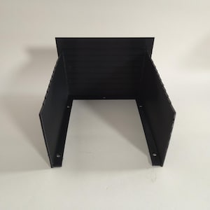 May include: A black, U-shaped bracket with a flat top and angled sides. The bracket has a series of horizontal lines on the top section and holes on the bottom for mounting. The bracket is made of a rigid material.