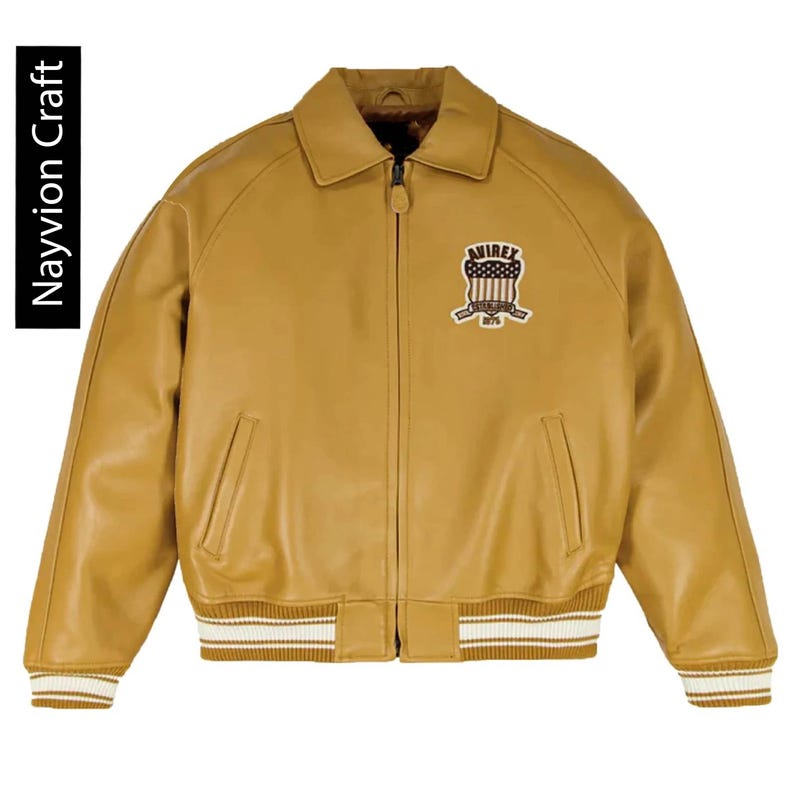 May include: Mustard-colored leather jacket with a collared neckline, a zipper closure, and two front pockets. The jacket features a patch on the chest with the text "AVIREX 1975". The cuffs and hem have white and tan striped detailing. The text "Nayvion Craft" is on the left side.