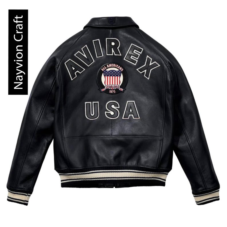 May include: Black leather jacket with white embroidered lettering and a patch featuring the American flag. The jacket has a classic bomber style with a ribbed hem and cuffs. The text "AVIREX" and "USA" are prominently displayed.