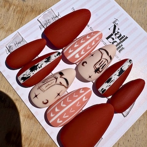 May include: A set of press-on nails in various designs. Some nails are solid matte red, while others feature patterns like white chevrons on a peach background, and black and white abstract designs. The Nail Edit logo is visible.