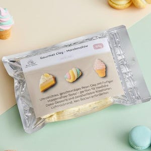 Könnte beinhalten: Ein silberner Folienbeutel mit Gourmet Clay, beschriftet als Marshmallow, mit 30g Inhalt. Die Verpackung zeigt Bilder eines Kuchenstücks, eines Marshmallows und einer Eistüte. Um den Beutel herum liegen zwei Windbeutel und zwei Macarons.