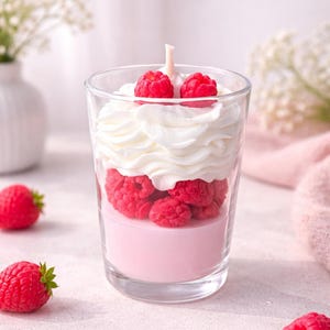May include: A glass candle featuring a base of solid light pink wax, a middle layer of red raspberry-shaped wax pieces, and a top layer of white whipped wax with two red raspberry-shaped wax pieces and a single centred cotton wick.