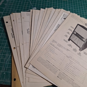 May include: A collection of vintage paper documents, including a "PHOTOFACT Folder" and schematics for electronics. The papers are off-white with black text and illustrations, featuring brands like Emerson and Sears Silvertone. Some pages have hole punches.