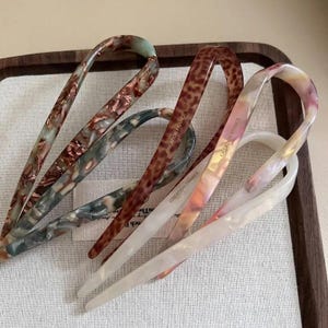 Puede incluir: Cuatro horquillas para el pelo en forma de U hechas de acetato de celulosa con varios patrones, incluyendo estampado de leopardo marrón, verde jaspeado, marrón jaspeado y blanco nacarado. Cada horquilla tiene el texto CREATION FRANCE.