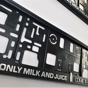 May include: Black license plate frame with silver lettering that reads "ONLY MILK AND JUICE". The frame features various cut-out shapes and the text "COME IN 2 LITRES".